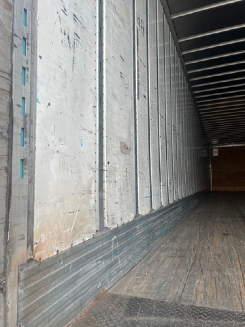 Trailer interior showing metal walls and wooden floor of a cargo area with sidewall vertical ribs.