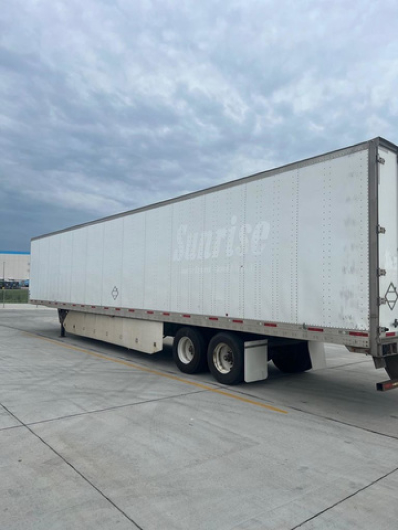 Trailer of a utility van with a faded 'Sunrise' logo on the side, showing a side view of a long silver trailer with two rear axles and a storage box underneath.