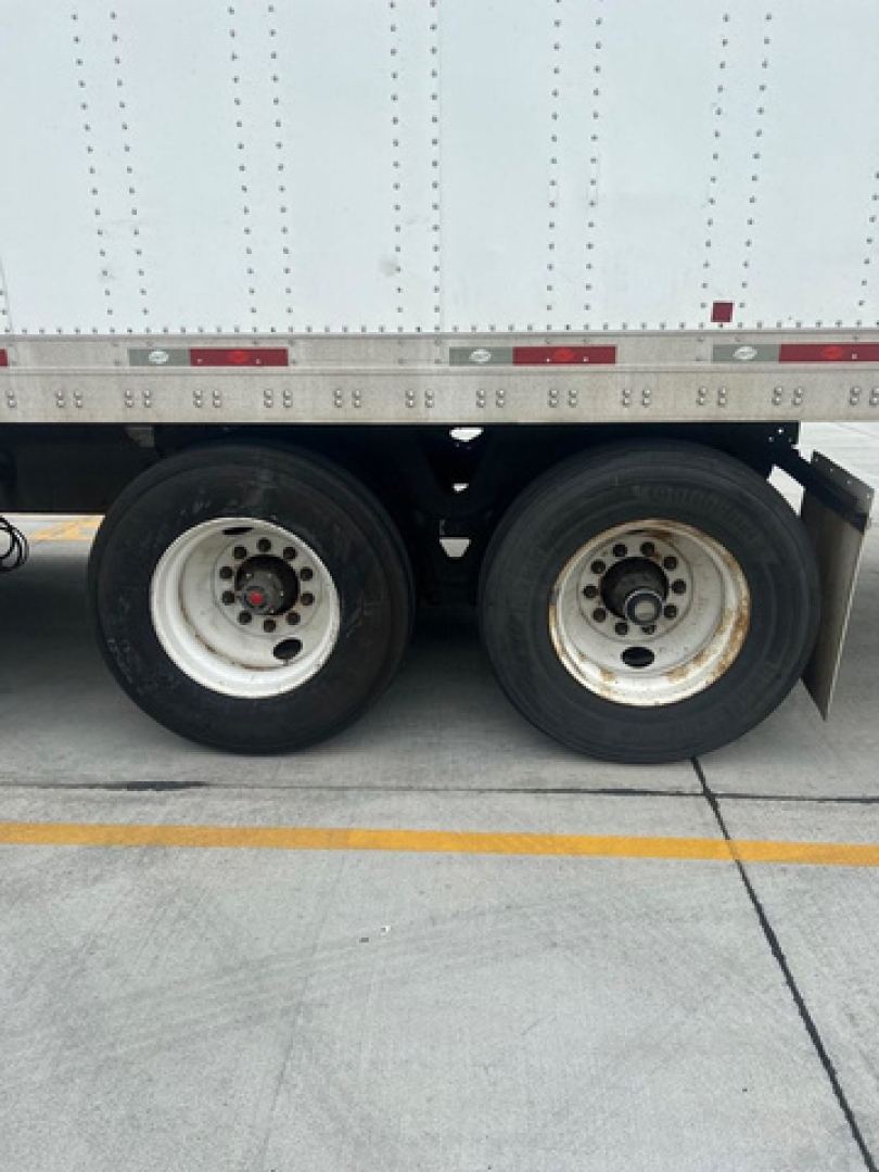 Rear wheels of a utility trailer with white cargo container, two axles, with tires and rims visible.
