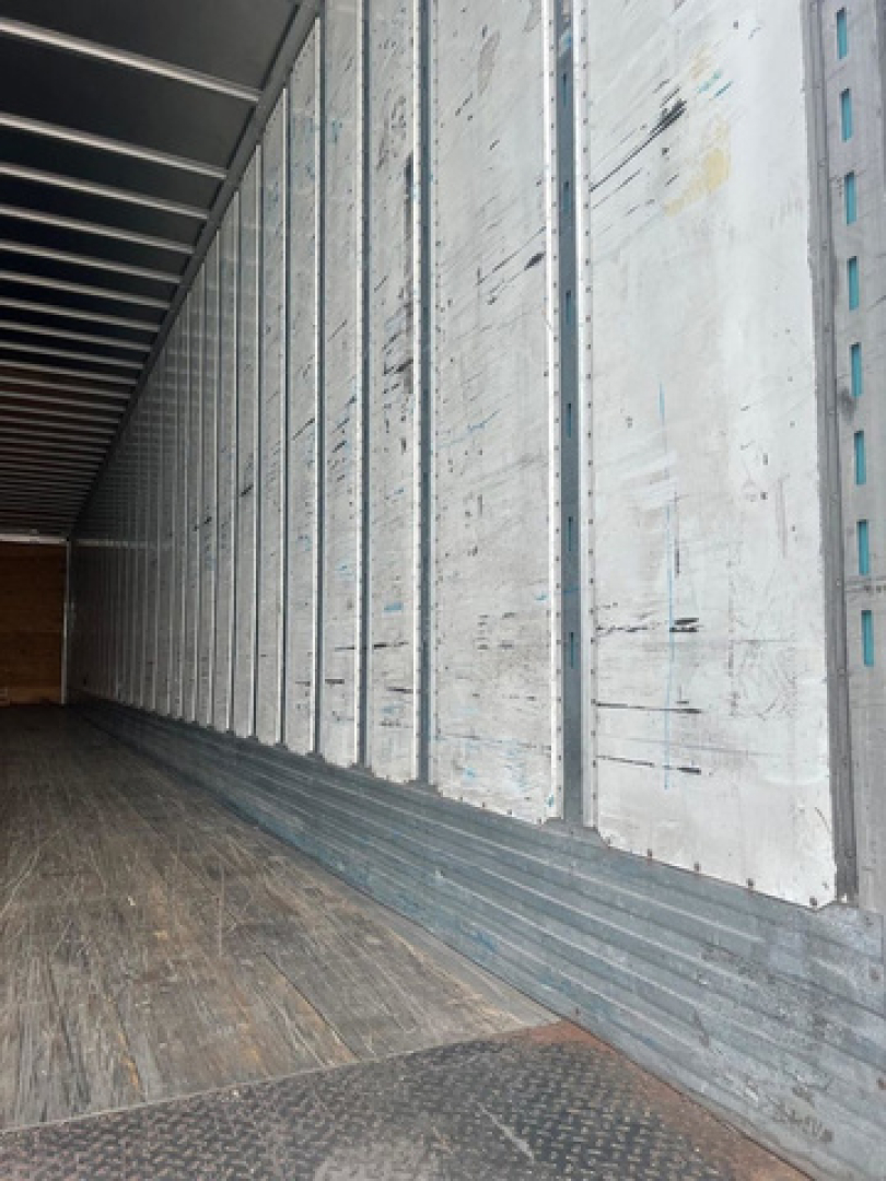 Trailer interior showing vertical metal walls and wooden floor of a cargo area.