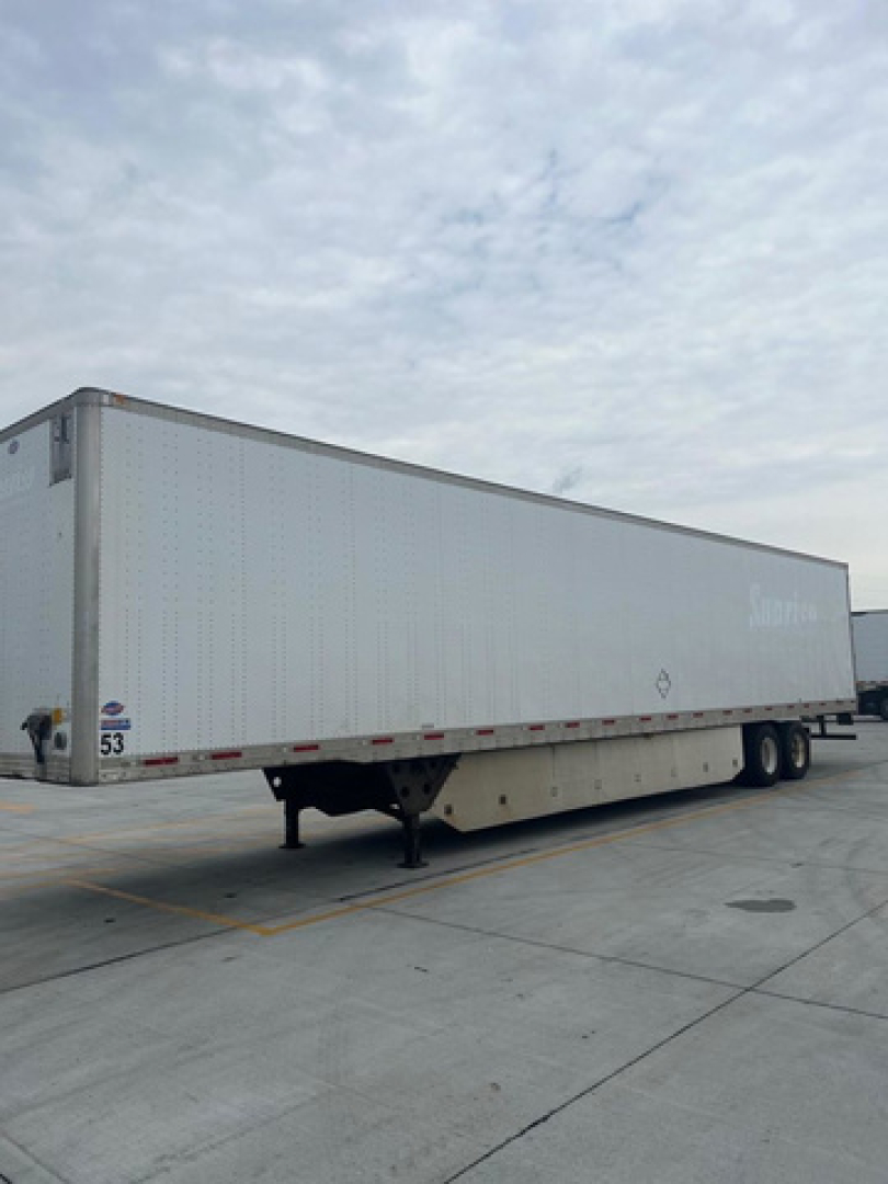 Utility van trailer side view showing a long white dry van with tandem axles and landing gear.