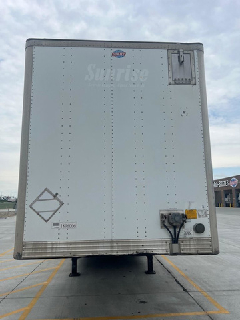 Rear of a white utility van trailer with a small logo near top, a black chute, and access doors; cargo area showing riveted panels and stabilizing legs under trailer