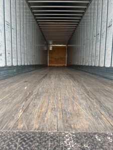 Trailer interior showing empty cargo area with wooden floor and metal sidewalls, front bulkhead visible at far end.