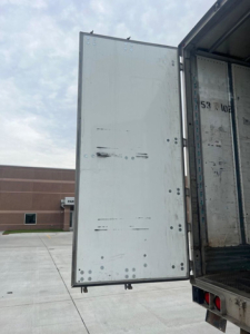 Trailer rear door showing metal surface with multiple welds and small black marks.