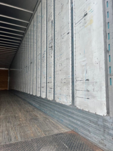 Trailer interior showing vertical metal walls and wooden floor of a cargo area.
