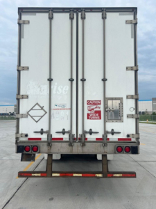 Rear view of a white utility van trailer with double doors, safety stickers, and latching hardware.