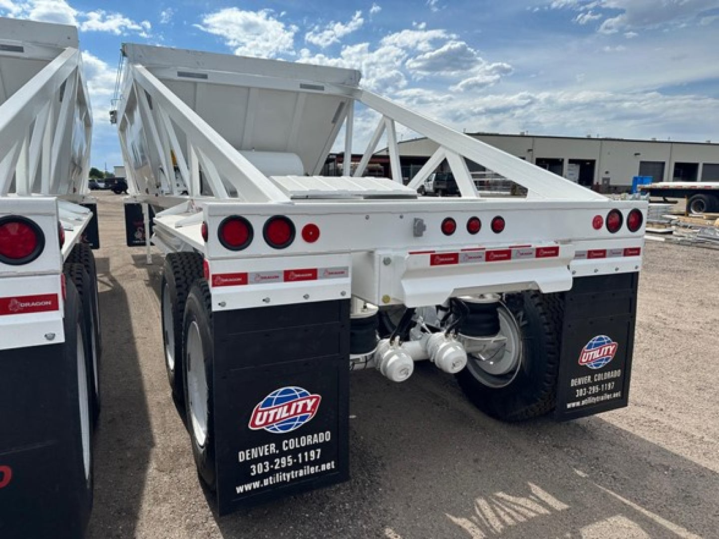 Rear view of a white 2026 Ranco Air Ride bottom dump trailer showing dual axles, black mud flaps with Utility Denver Colorado stickers, and red and white reflective tape.
