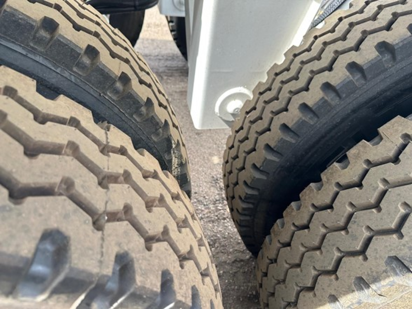 Bottom dump trailer axle area showing dual rear tires with tread patterns and a white frame component between the tires.