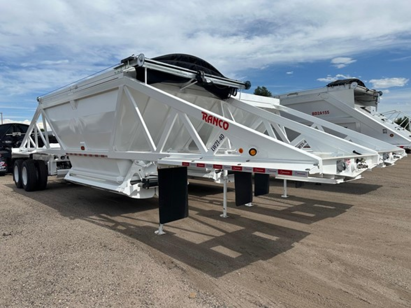 Bottom dump trailer by Ranco with white chassis and lattice framework, tandem axle, hydraulic hopper. Visible 'RANCO' branding on side.