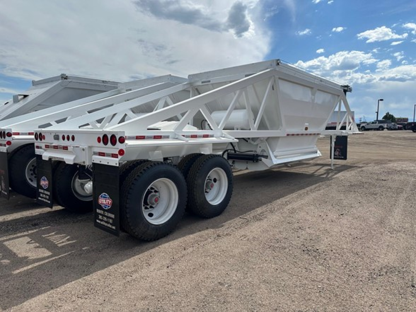 Ranco air ride bottom dump trailer showing white framework and tandem axle wheels with black tires; side steel ramps and rear lights visible.