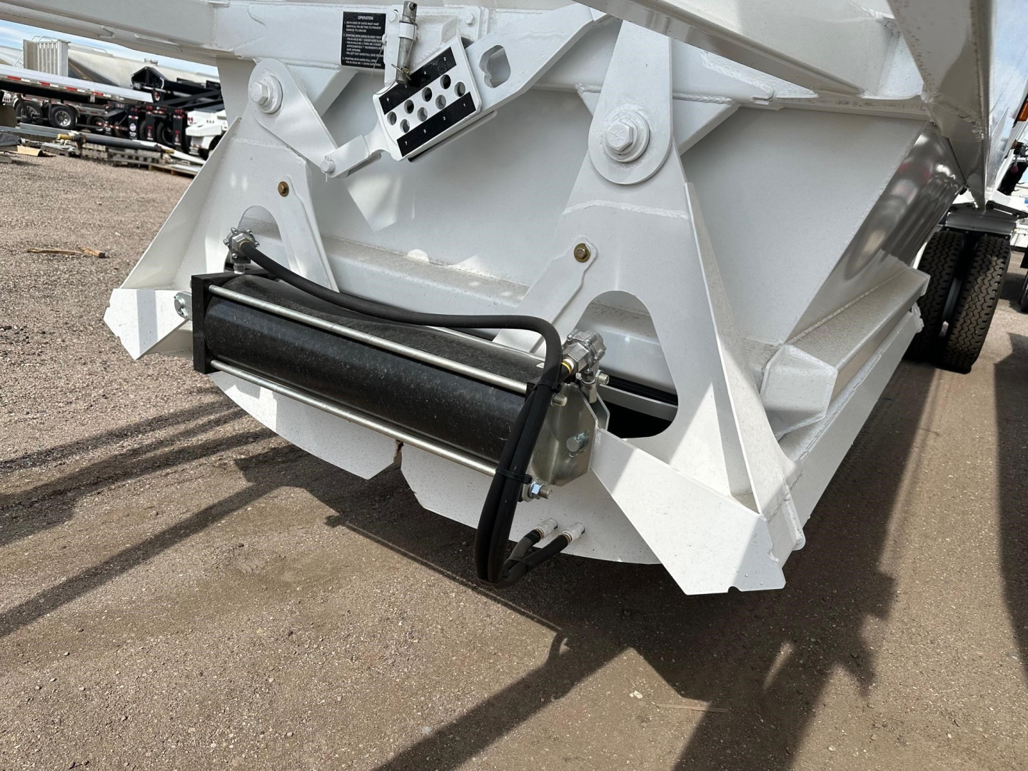 Ranco air ride bottom dump trailer showing hydraulic cylinder and mounting hardware with white painted steel frame and hinge area.