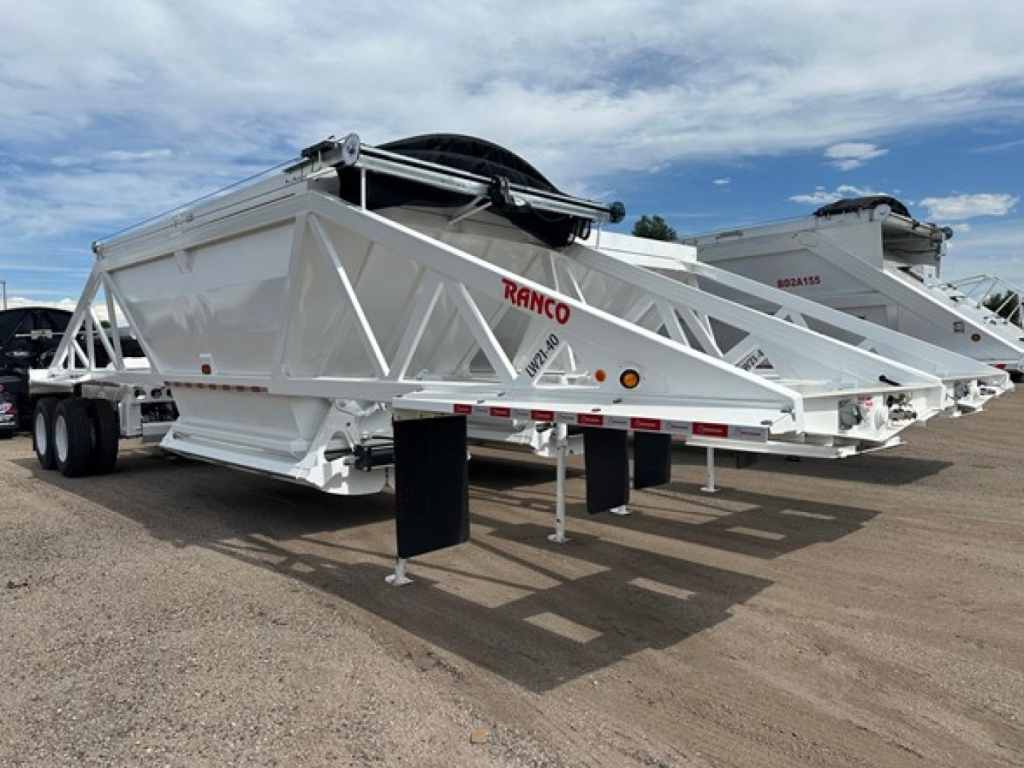 Bottom dump trailer by Ranco with white chassis and lattice framework, tandem axle, hydraulic hopper. Visible 'RANCO' branding on side.