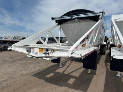 Trailer front section showing Ranco air ride bottom dump trailer with triangular frame, white paint, spare tire mounted on top, safety chains, labels and hydraulic components visible on the front rail.