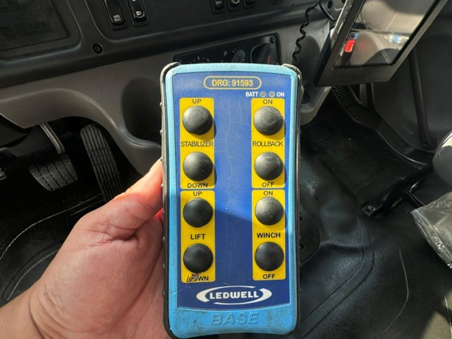 Control pendant with blue housing showing DRG:91593 label and yellow buttons labeled UP STABILIZER, DOWN UP, LIFT, BATT ON, ROLLBACK ON, WINCH OFF, LEDWELL BASE.