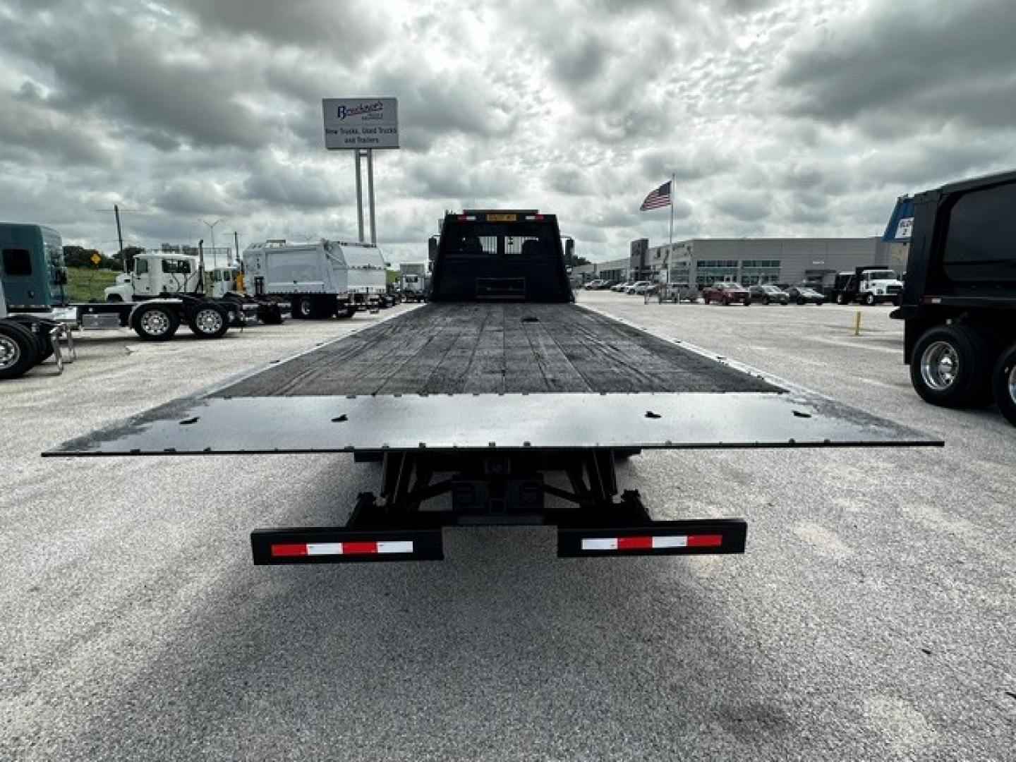 Flatbed tow truck bed with a low rear view, Freightliner M2106 in a dealership lot, ramp extended, rear bumper lights visible.