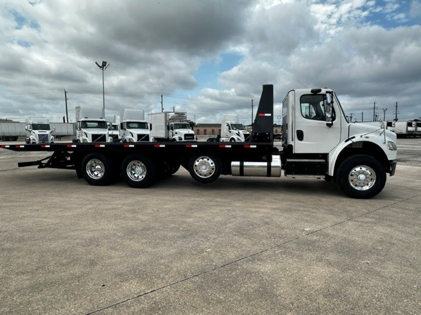 Freightliner M2106 rollback truck side view showing flatbed with three axles and white cab.