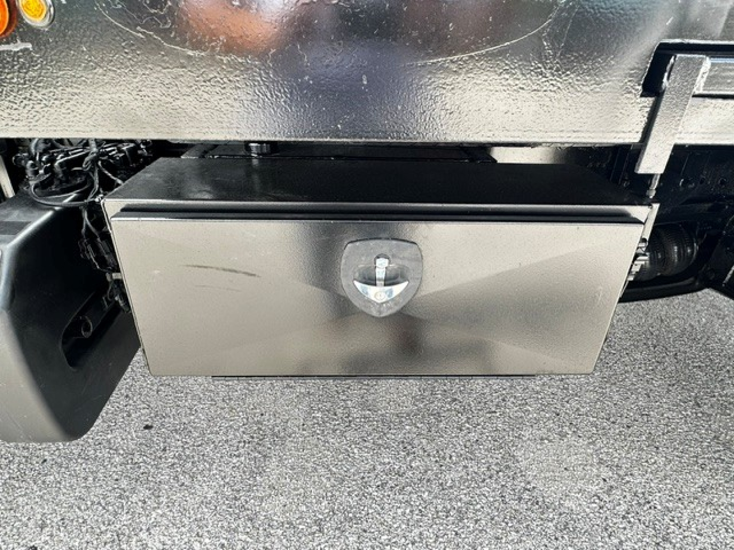 Metal toolbox under Freightliner M2106 chassis showing a rectangular silver tool box with a central latch.