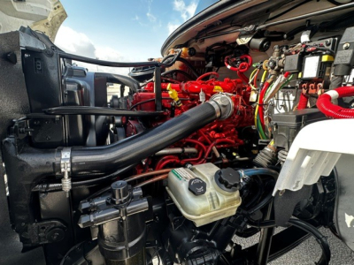 Freightliner M2106 engine bay showing red engine components, black air intake hose, coolant reservoir, and various wiring harnesses.