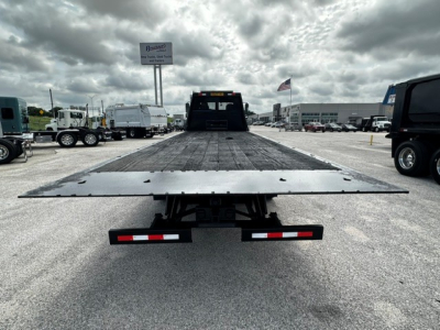 Flatbed tow truck bed with a low rear view, Freightliner M2106 in a dealership lot, ramp extended, rear bumper lights visible.