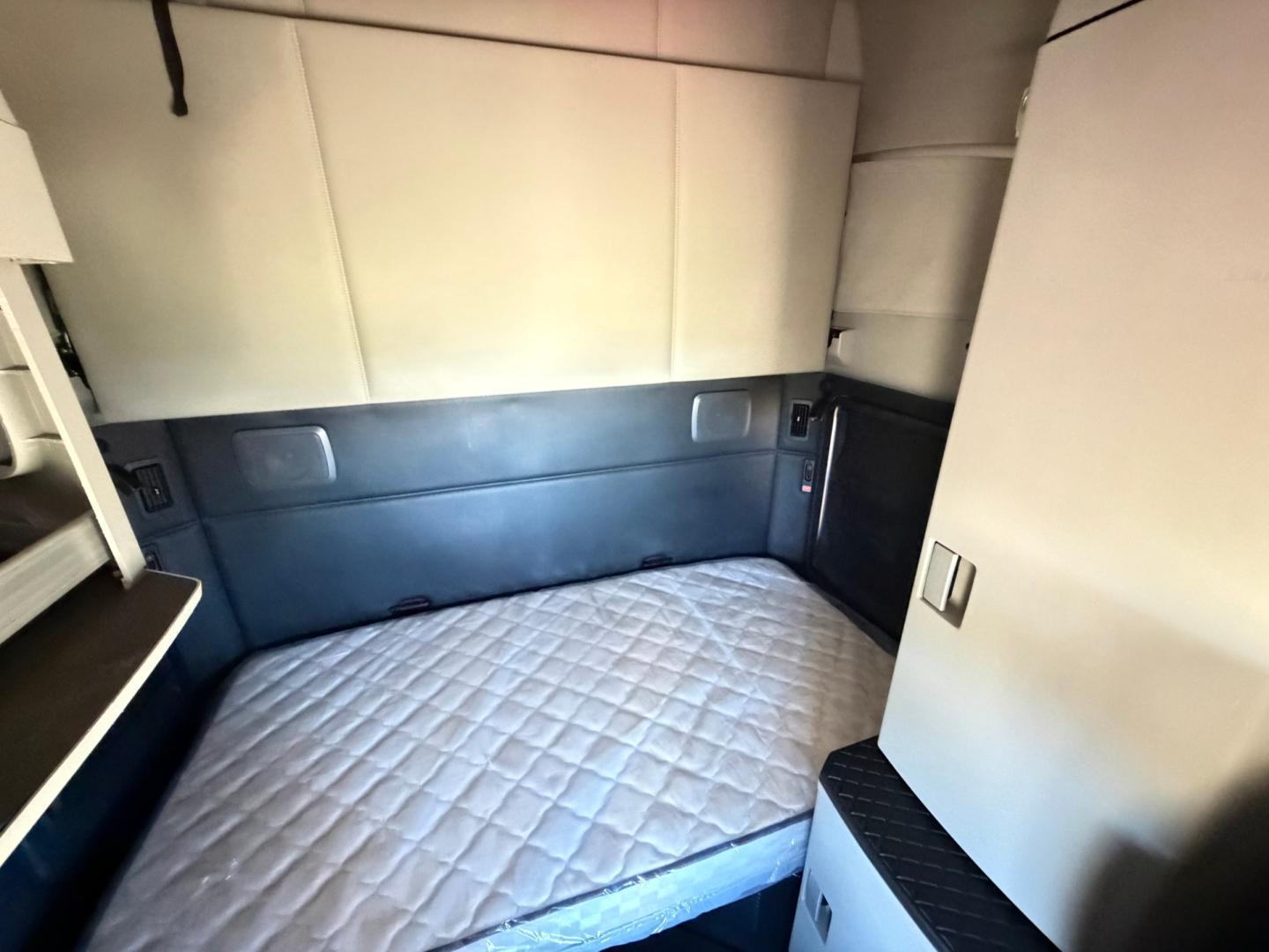 Kenworth T680 sleeper cab interior showing bed area with quilted mattress and storage cabinets.