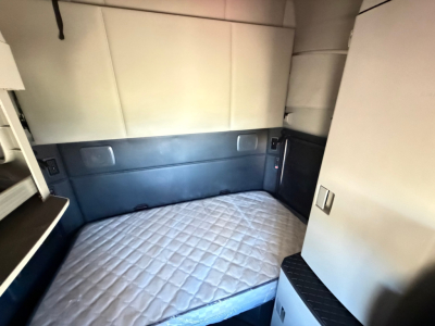 Kenworth T680 sleeper cab interior showing bed area with quilted mattress and storage cabinets.