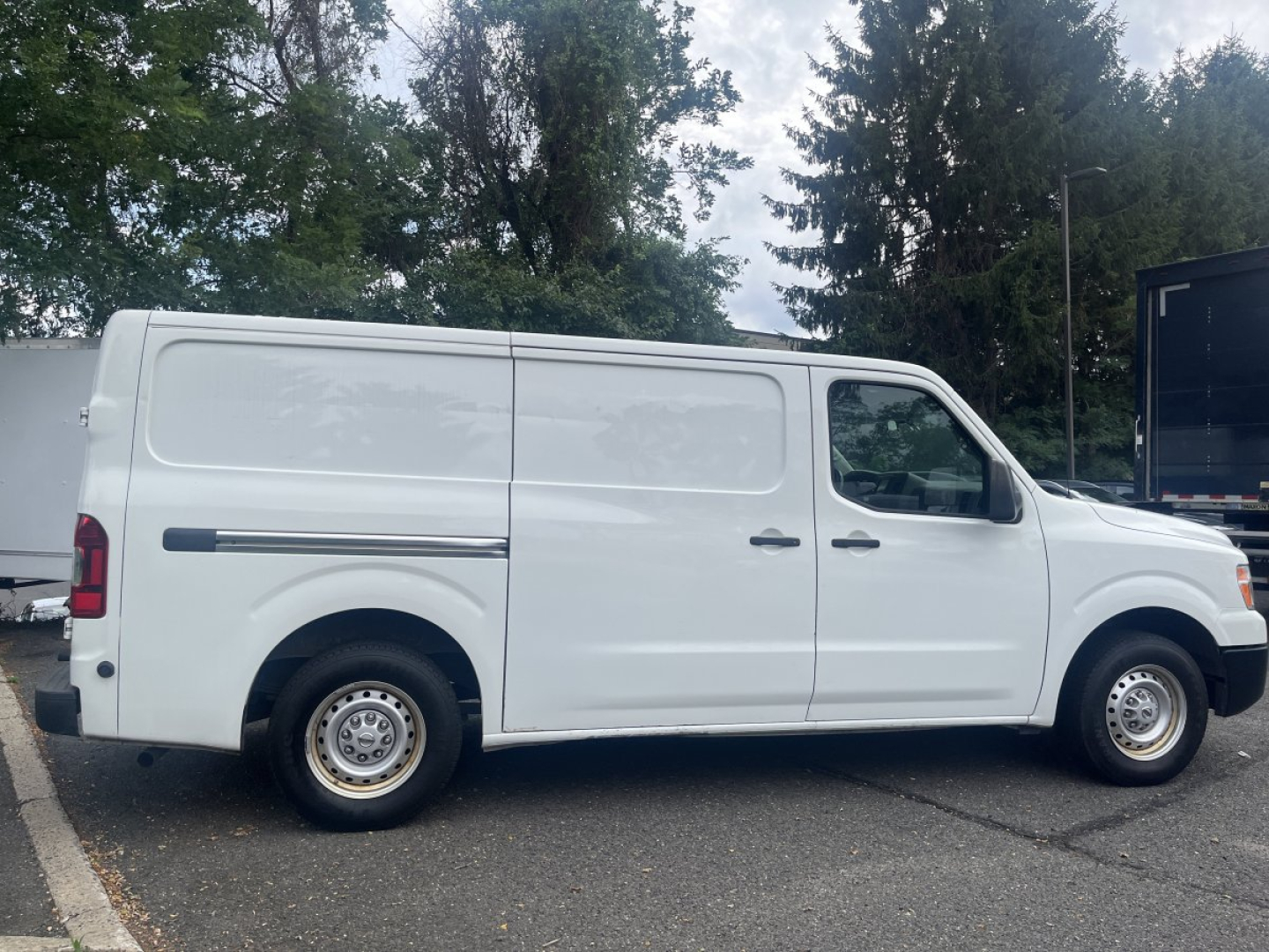 Side view of a white 2019 Nissan NV Cargo van in a parking lot.