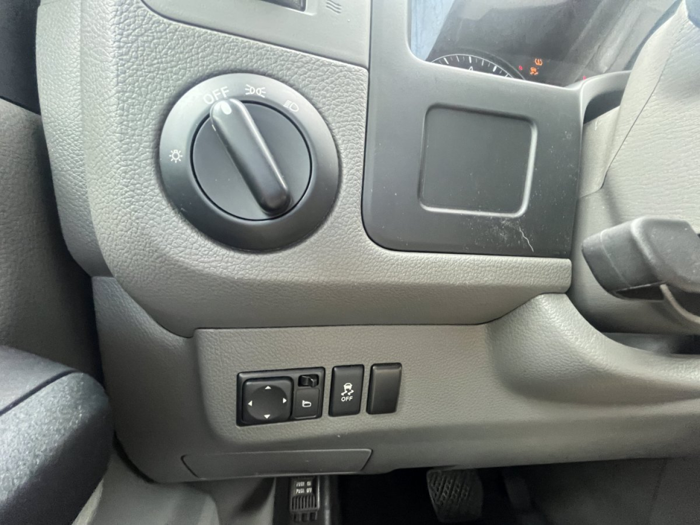 Dashboard area of a 2019 Nissan NV Cargo showing headlight switch and control panel with blank display and small buttons; no visible model badge.