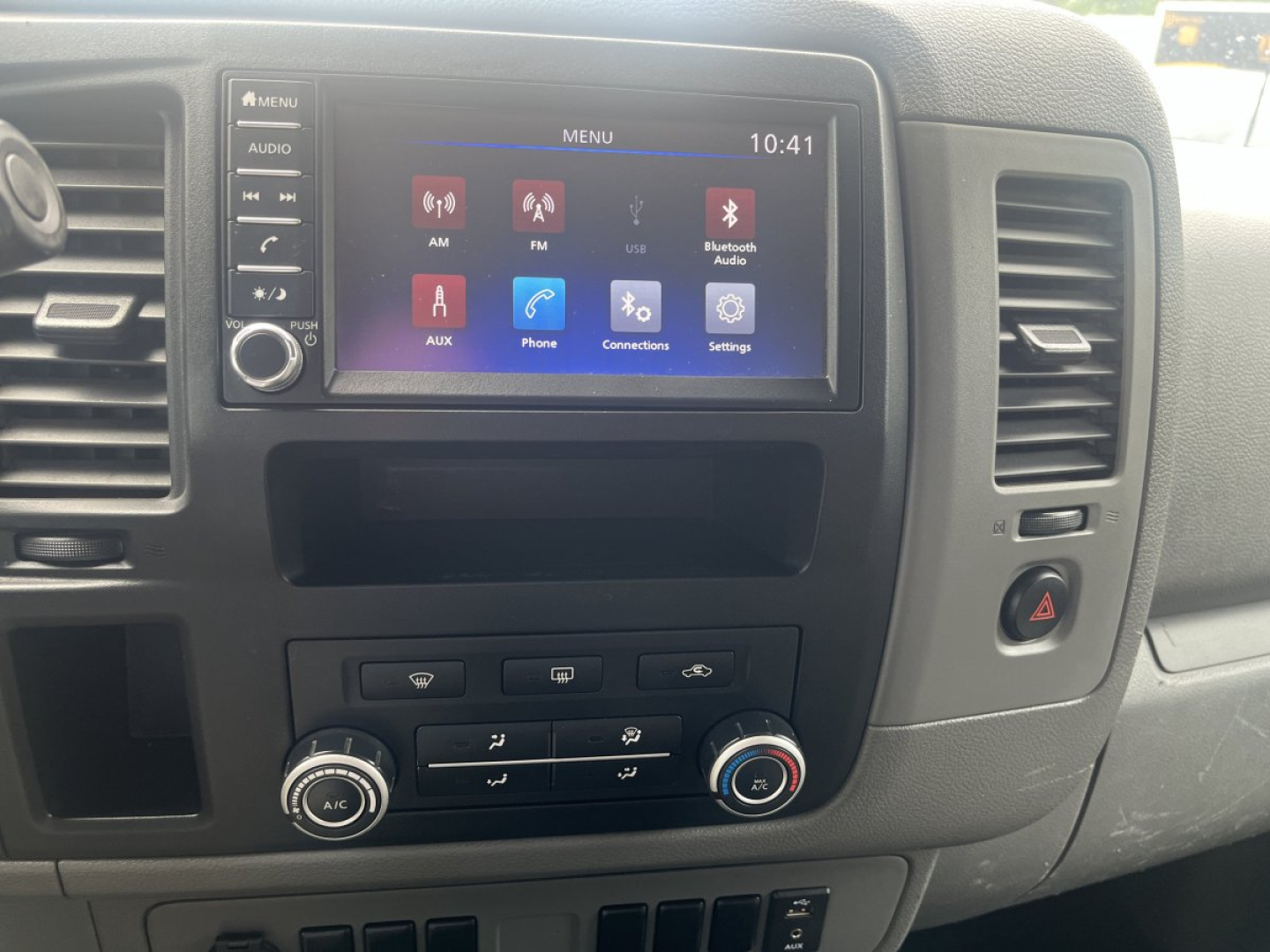 Dashboard of a 2019 Nissan NV Cargo showing the infotainment touchscreen with apps, climate controls, and hazard switch.