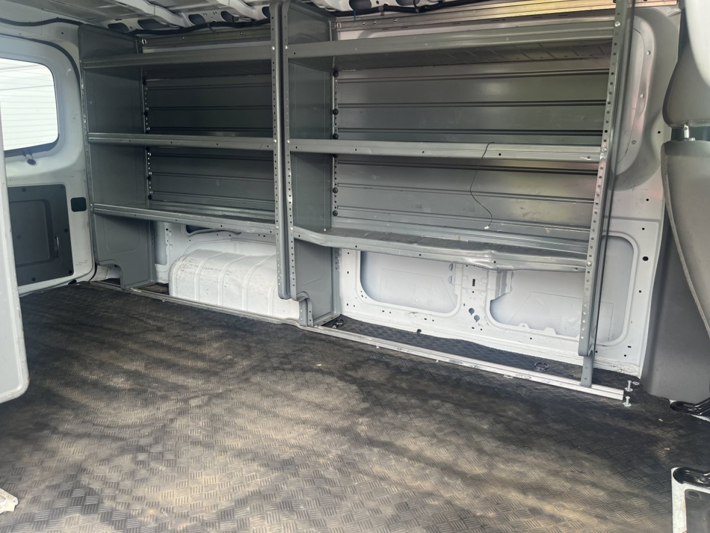 Nissan NV Cargo van interior showing metal shelving units along both walls in cargo area; empty cargo space with rubberized floor.