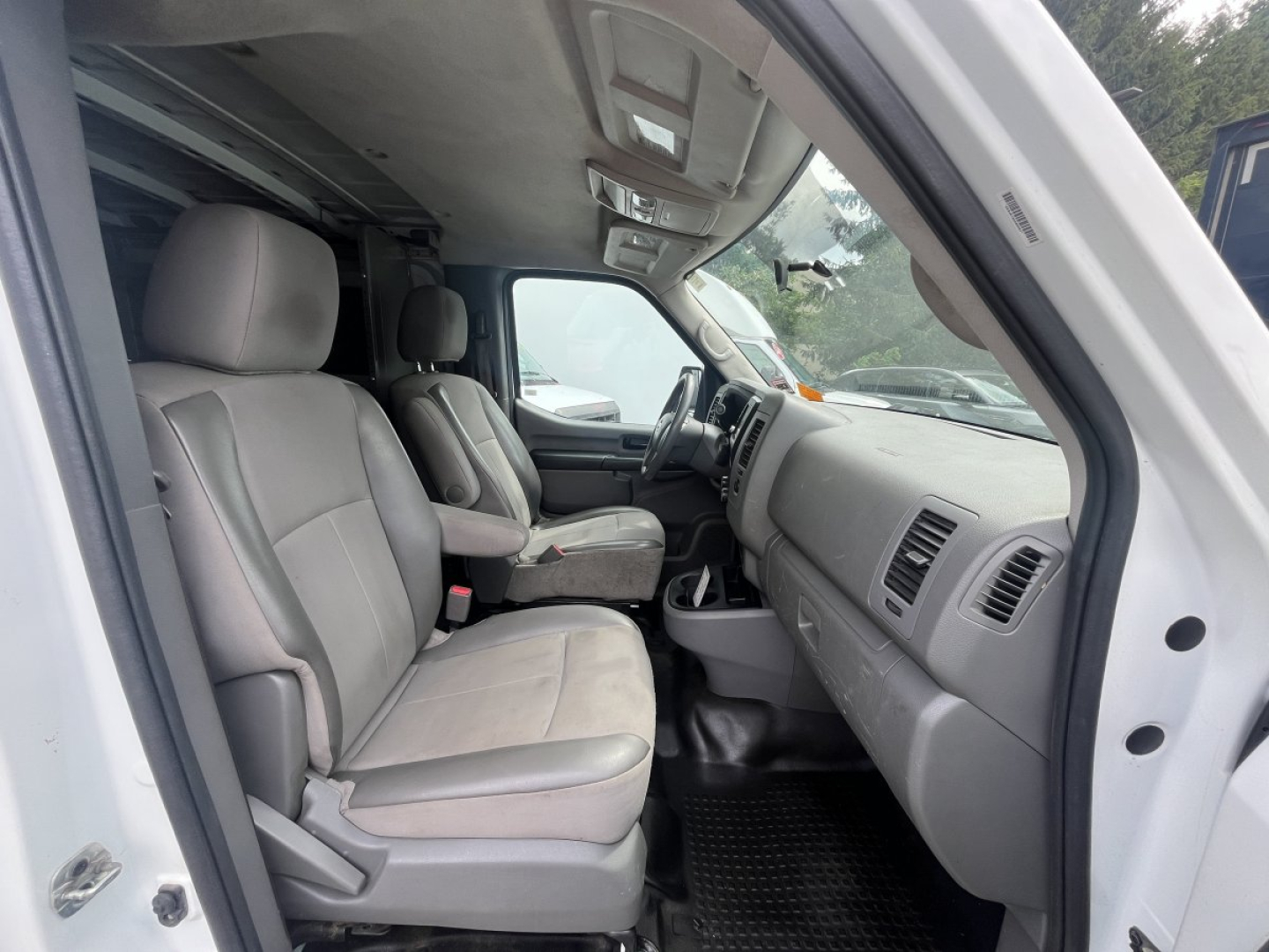 Nissan NV Cargo cab interior view showing front seats and dashboard from driver side door.