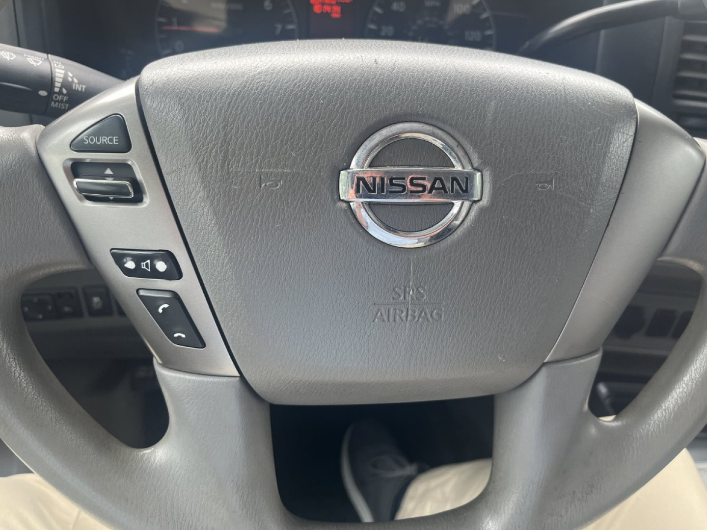 Nissan steering wheel with center emblem; left control buttons visible; dashboard in background.