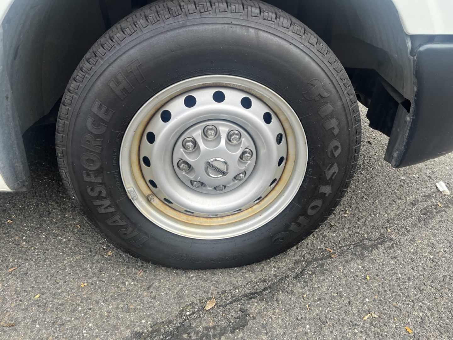Wheel and tire on Nissan NV Cargo showing Goodyear/Fleet tire with steel wheel and hub. Visible text: 'INSFONGE' or 'FIRESTONE' along sidewall, tire tread, and hubcap bolts.
