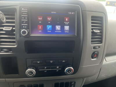 Dashboard of a 2019 Nissan NV Cargo showing the infotainment touchscreen with apps, climate controls, and hazard switch.