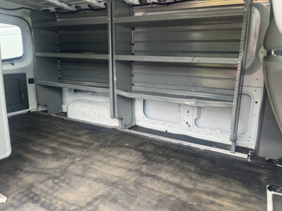 Nissan NV Cargo van interior showing metal shelving units along both walls in cargo area; empty cargo space with rubberized floor.