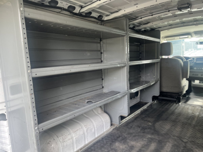 Nissan NV Cargo van interior showing metal shelving and storage racks along both sides, with a gray rubberized floor and passenger cockpit visible in background.