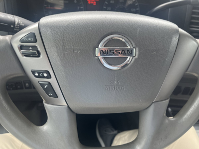Nissan steering wheel with center emblem; left control buttons visible; dashboard in background.