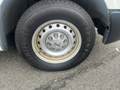 Wheel and tire on Nissan NV Cargo showing Goodyear/Fleet tire with steel wheel and hub. Visible text: 'INSFONGE' or 'FIRESTONE' along sidewall, tire tread, and hubcap bolts.