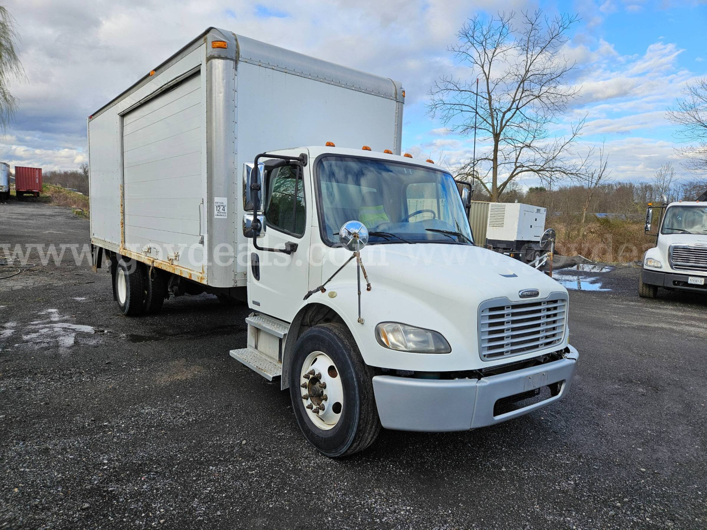 White Freightliner M2 106 box truck in a parking lot, side view showing cab, side mirrors, headlights, and cargo box; no legible labels or fluid markings visible.