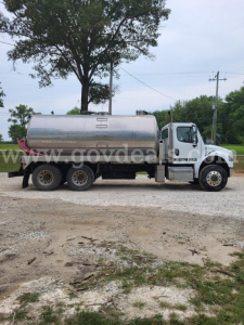 Freightliner M2 tanker truck side view showing stainless steel cylindrical tank and white cab.