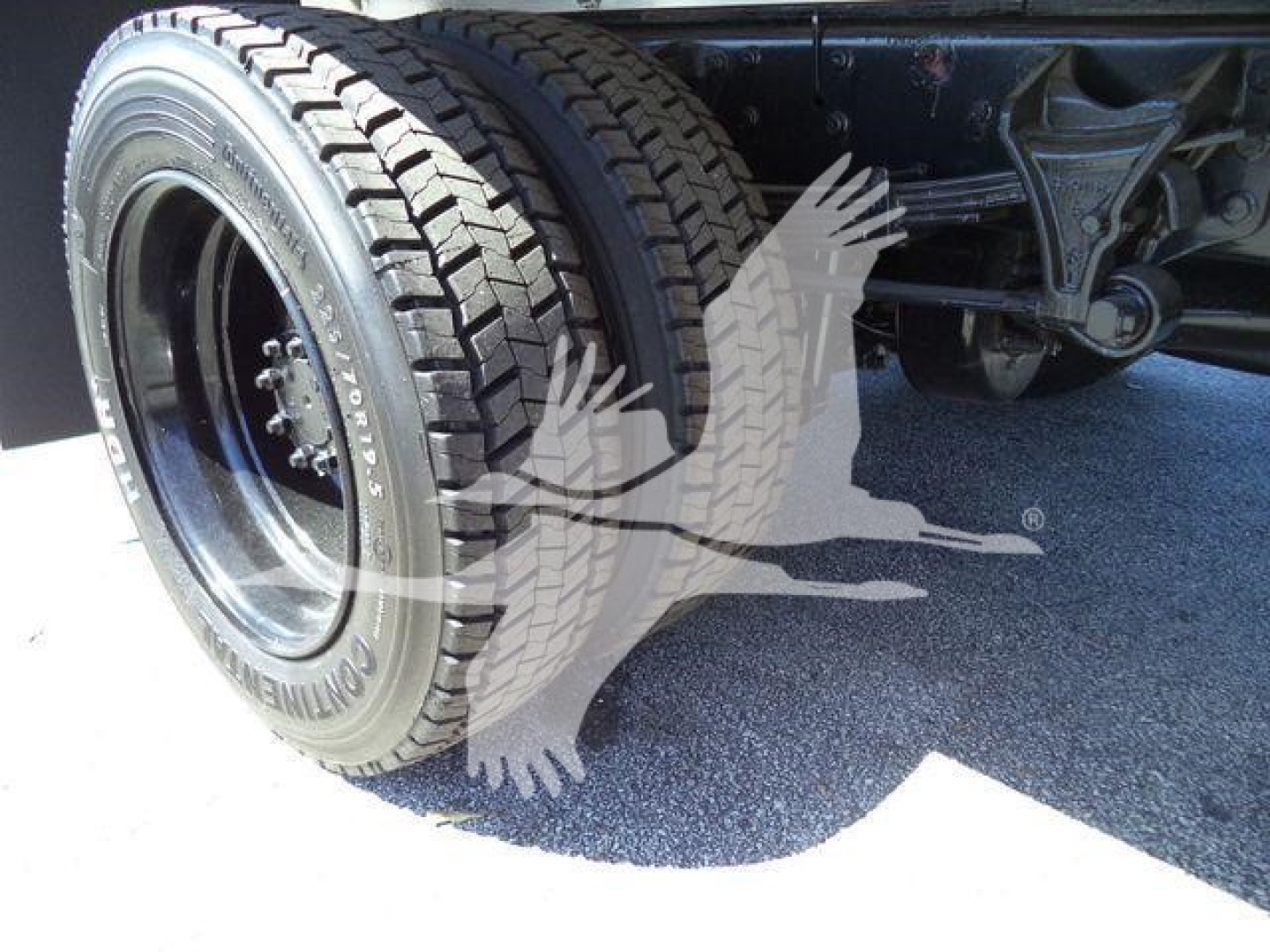 Truck wheel and rear suspension of a 2023 Chevrolet Silverado 6500HD flatbed truck showing dual rear tires and undercarriage components.