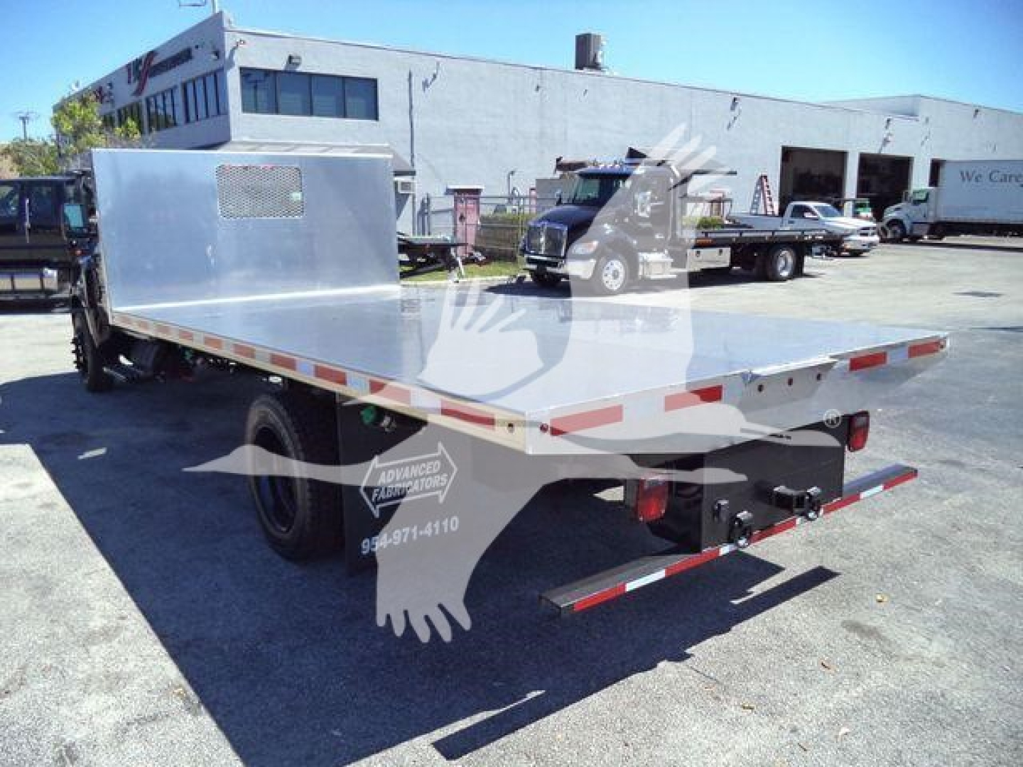 Flatbed tow truck bed with aluminum deck and rear bumper, Silverado chassis in background, stock number 6500ALUMFLAT, flatbed with reflective tape.