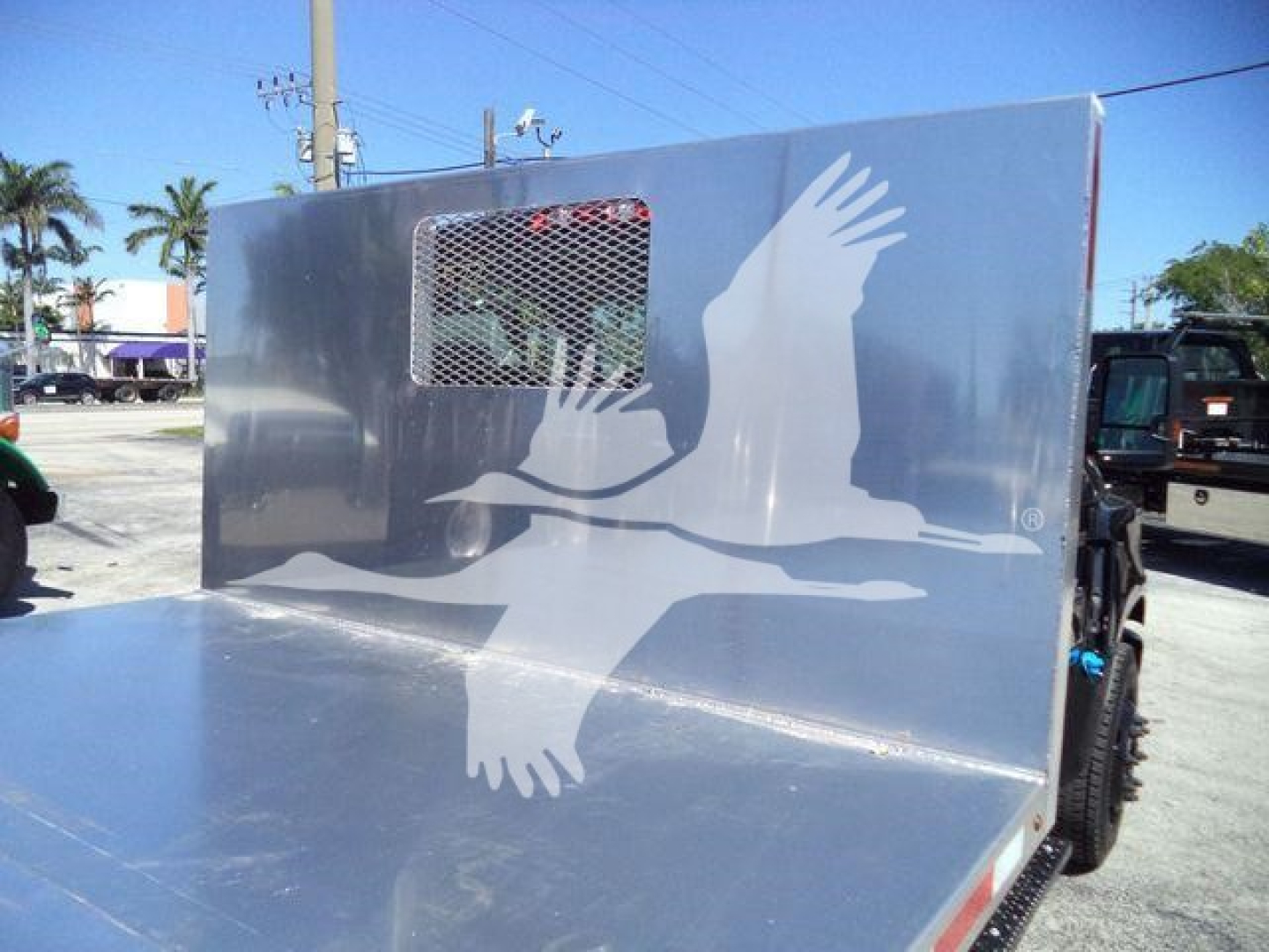 Flatbed truck with aluminum cab shield featuring a large white bird graphic and a vented window on the side.