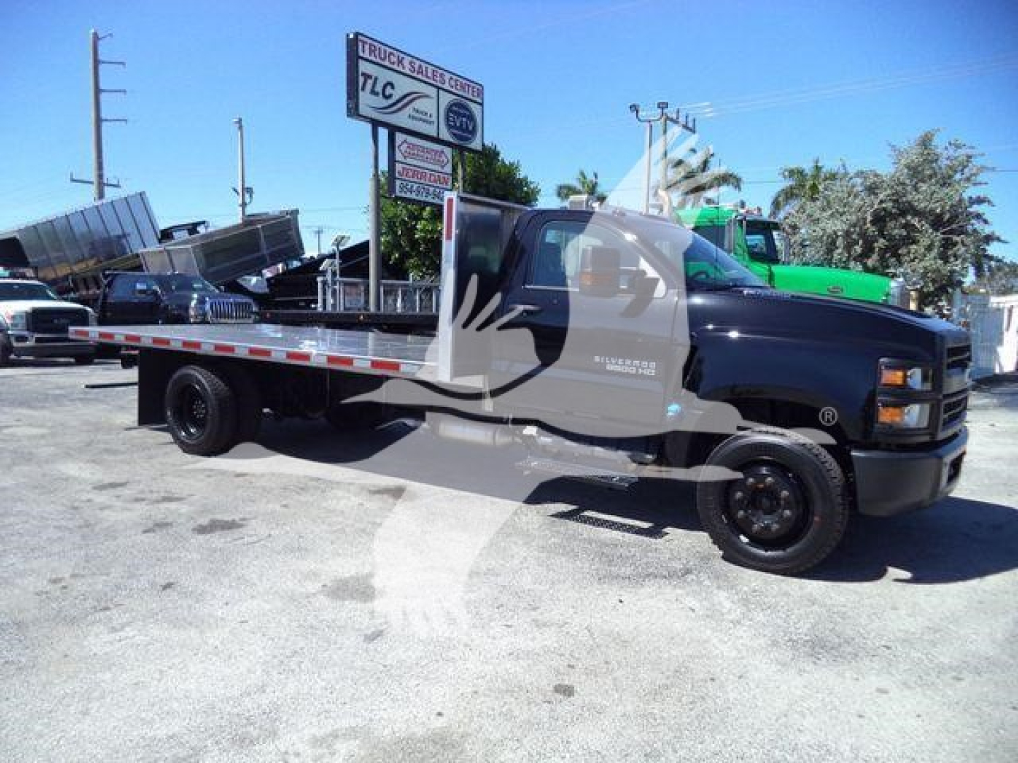 Flatbed tow truck/Chevrolet Silverado 6500HD side view showing flatbed bed and cab in a dealership lot.