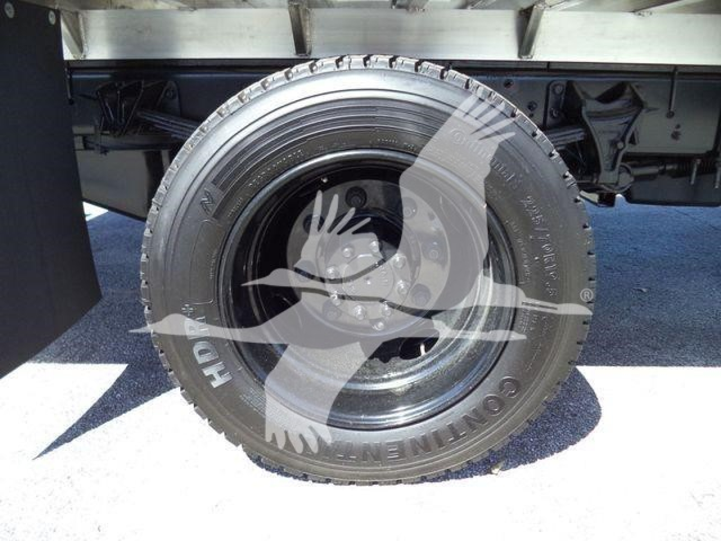Flatbed truck wheel showing Continental tire and spare under Chevrolet Silverado 6500HD chassis, undercarriage and part of flatbed frame visible.