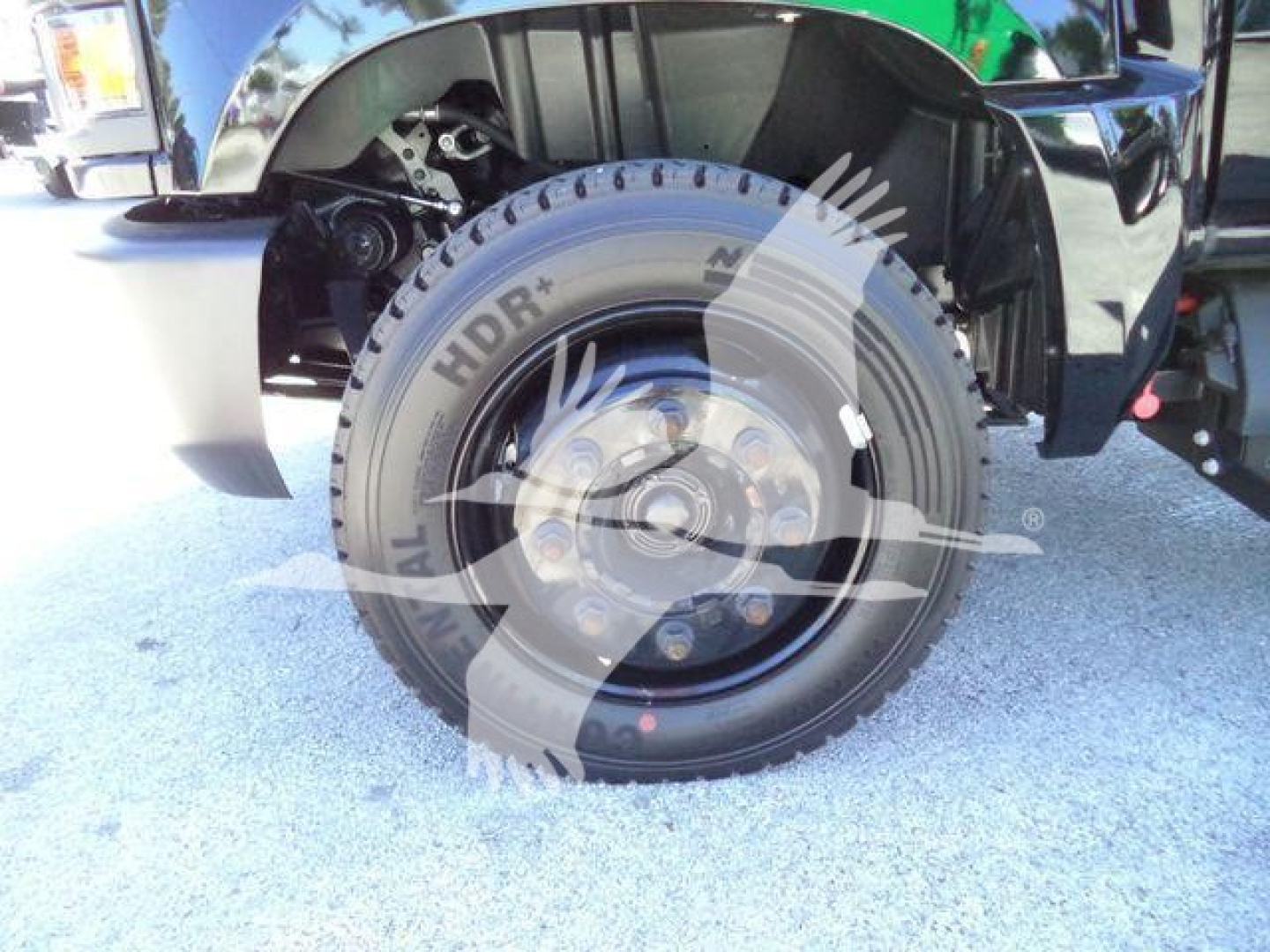 Chevrolet Silverado 6500HD flatbed truck wheel and front fender visible with tire branding. Wheel shows All Terrain, HDR+ marks and lug nuts; fender well and suspension components visible.