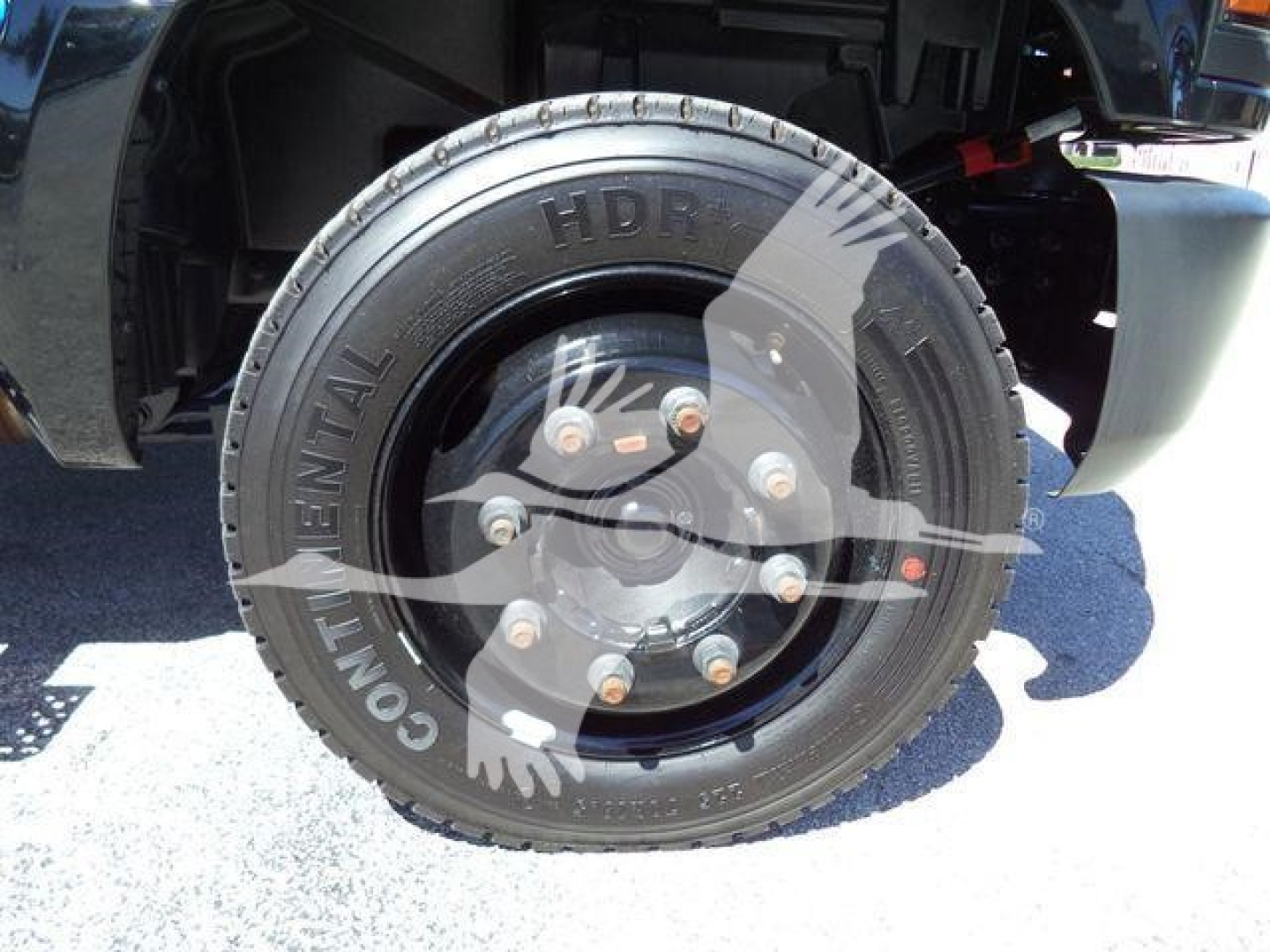 Truck wheel and tire close-up showing Continental tire with 'HD...', bolt pattern visible. Partial undercarriage of Chevrolet Silverado flatbed truck.