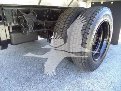 Truck rear axle area with dual rear wheels and flatbed frame; visible components include suspension linkage, leaf springs, and wheel tires.