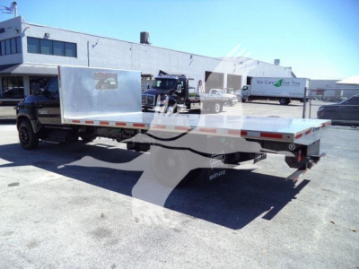 Flatbed tow truck trailer attached to Silverado 6500HD in showroom lot; side rails and wheel area visible.