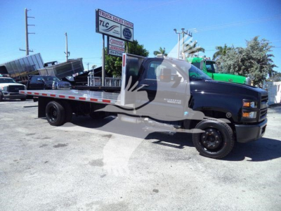 Flatbed tow truck/Chevrolet Silverado 6500HD side view showing flatbed bed and cab in a dealership lot.