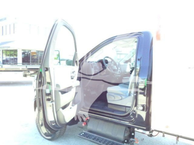 Truck cab interior with front passenger door open, showing steering wheel and dashboard in view; exterior black body with steps visible.